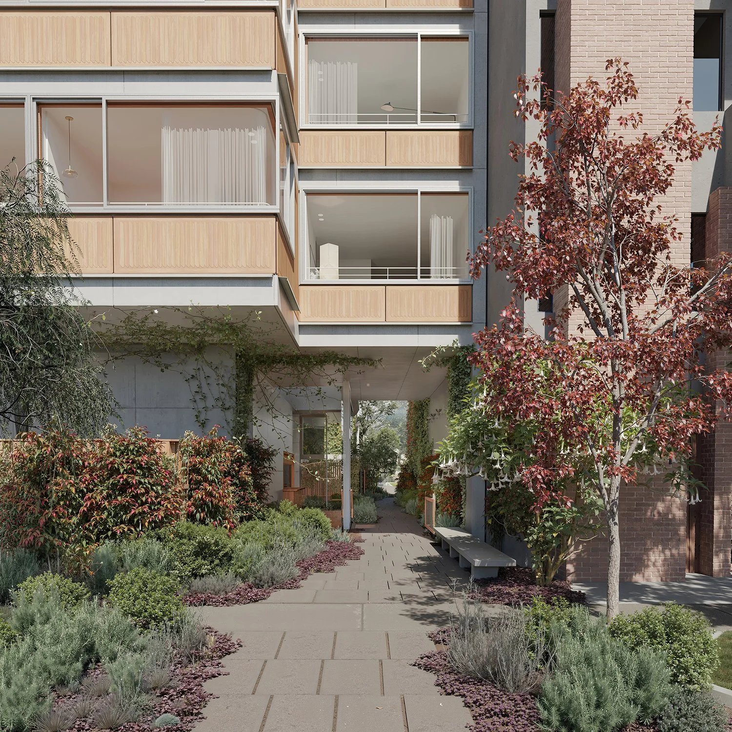 Pasillo de viviendas con jardines a ambos lados y una banca, con árboles de hojas rojas y plantas verdes alrededor.
