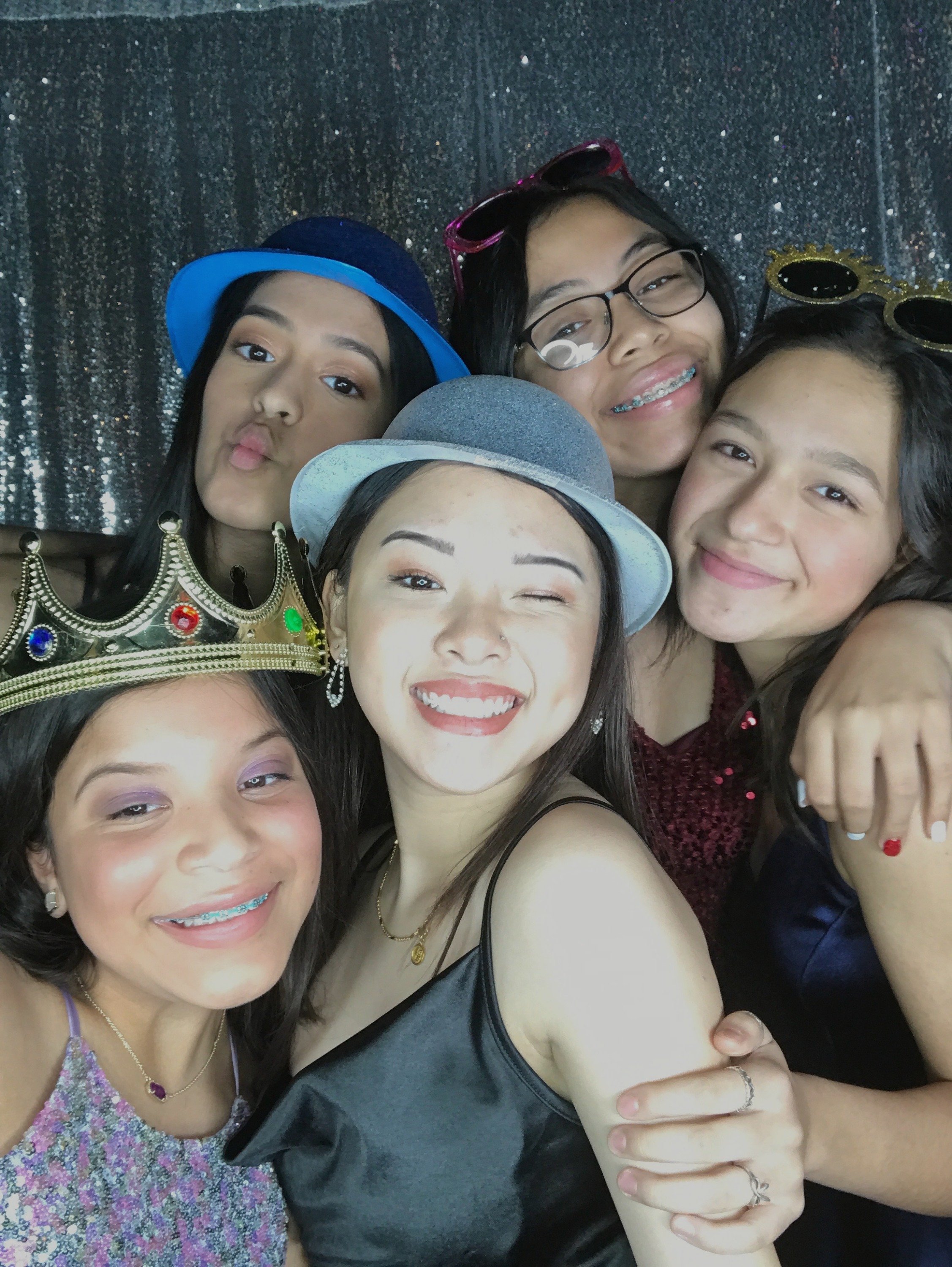 Group of five young women posing together, wearing various hats and accessories, smiling and enjoying themselves at a photo booth event.
