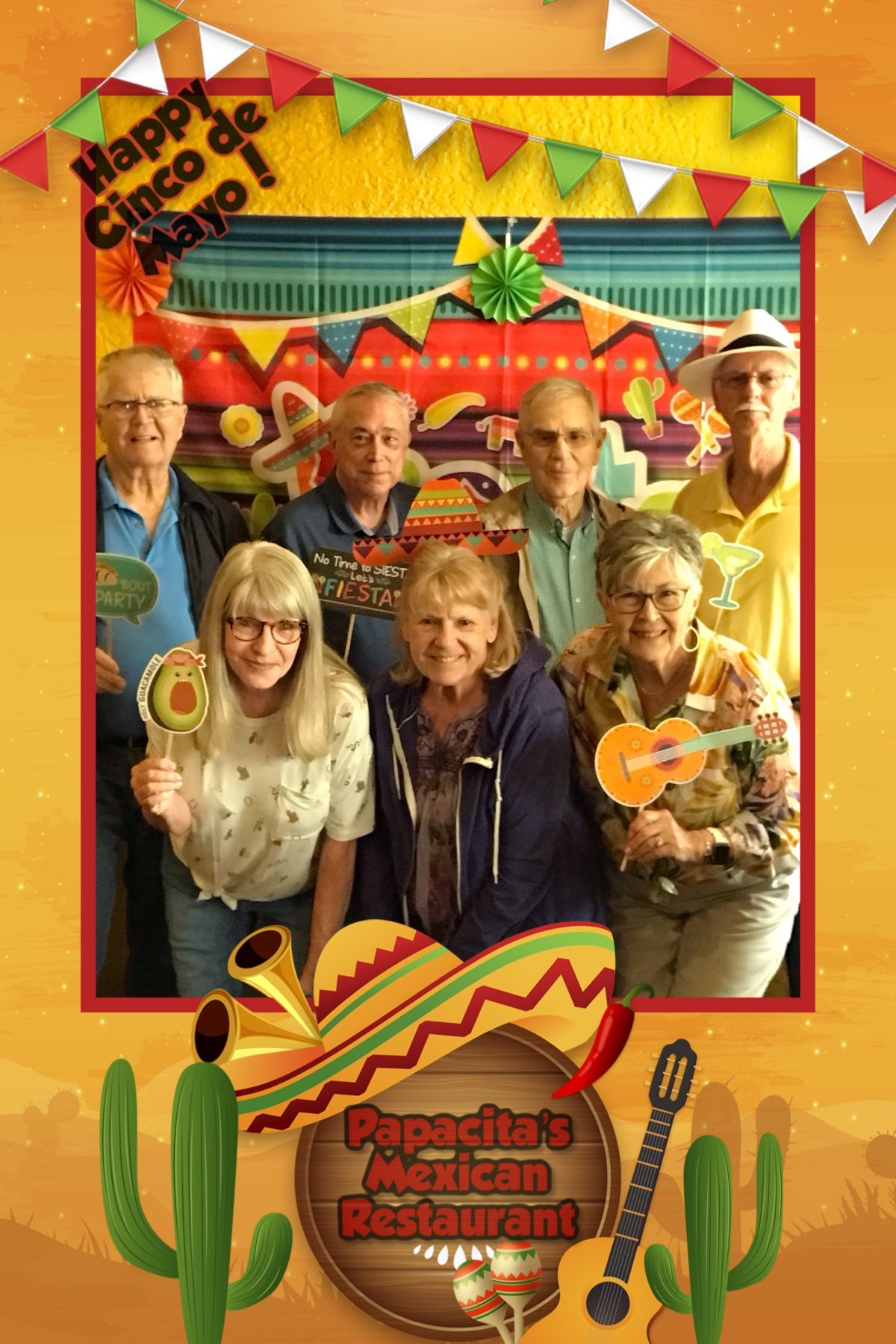 Group of people celebrating Cinco de Mayo at Papacita's Mexican Restaurant, holding festive props with a colorful backdrop.
