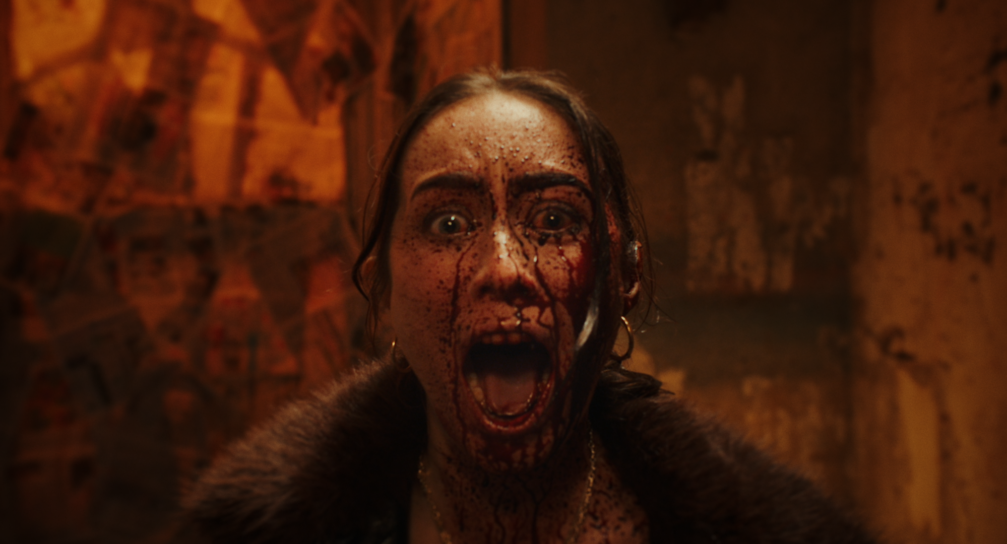A woman with makeup resembling blood and scars, screaming with mouth wide open, in a dimly lit, horror-themed setting.