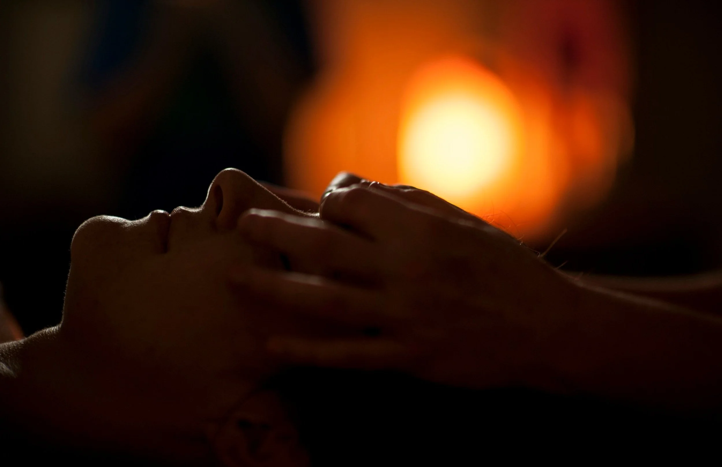 Silhouette of a person receiving a facial massage with warm, blurred lights in the background creating a relaxing atmosphere.