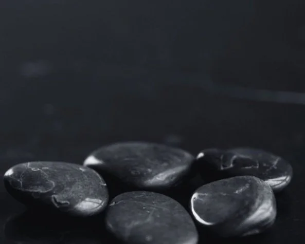 Smooth black stones on a dark background, arranged in a cluster.