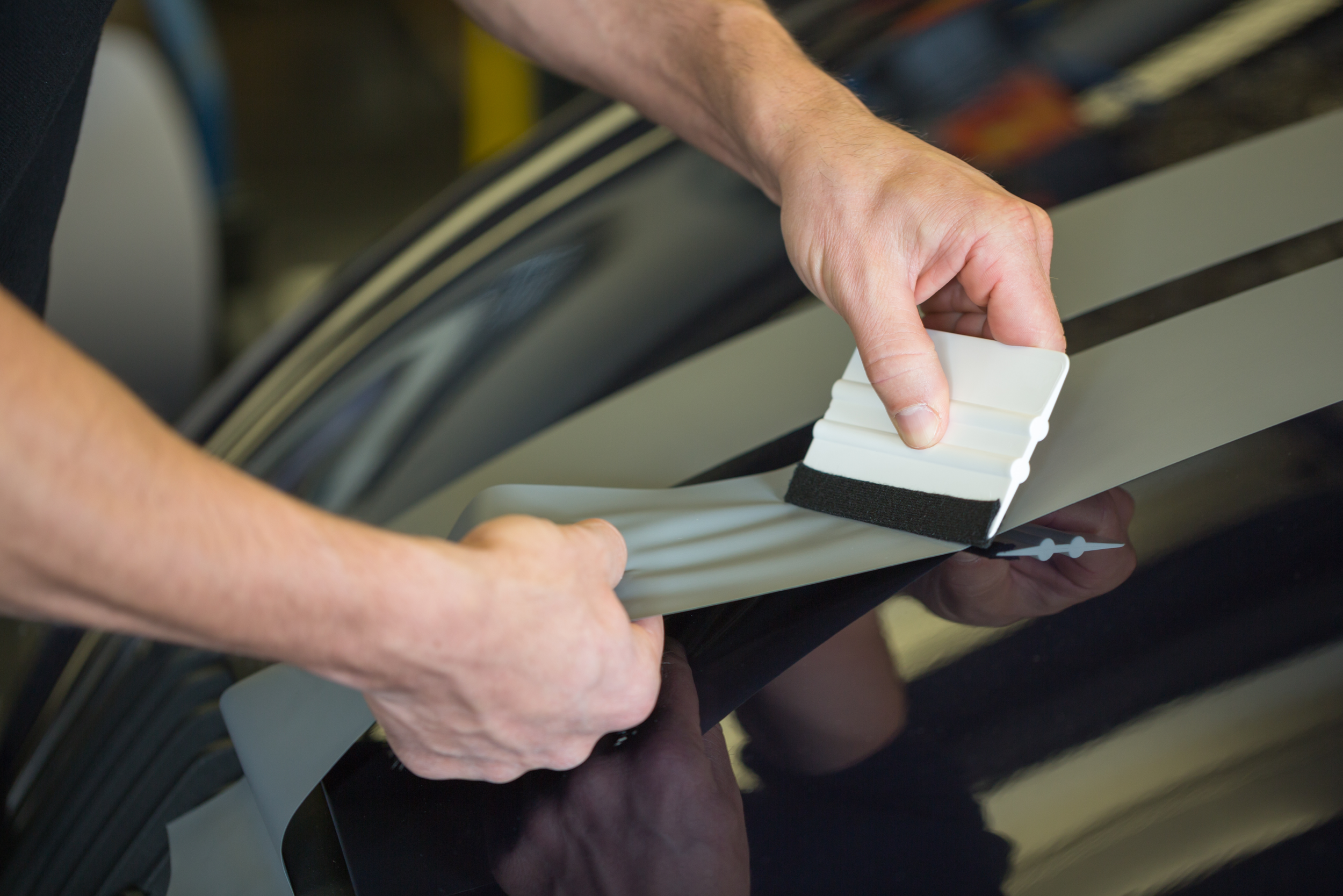 Person applying a vinyl decal to a car door using a squeegee.