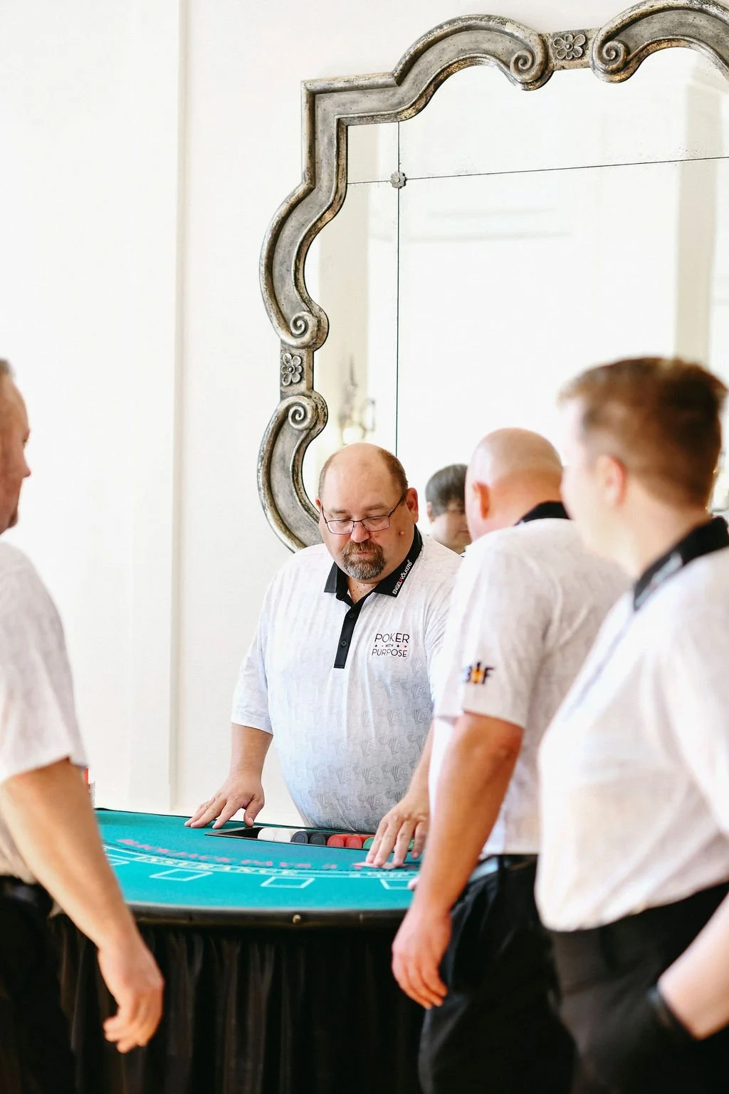 A group of men playing poker around a poker table, with a decorative mirror on the wall behind them.