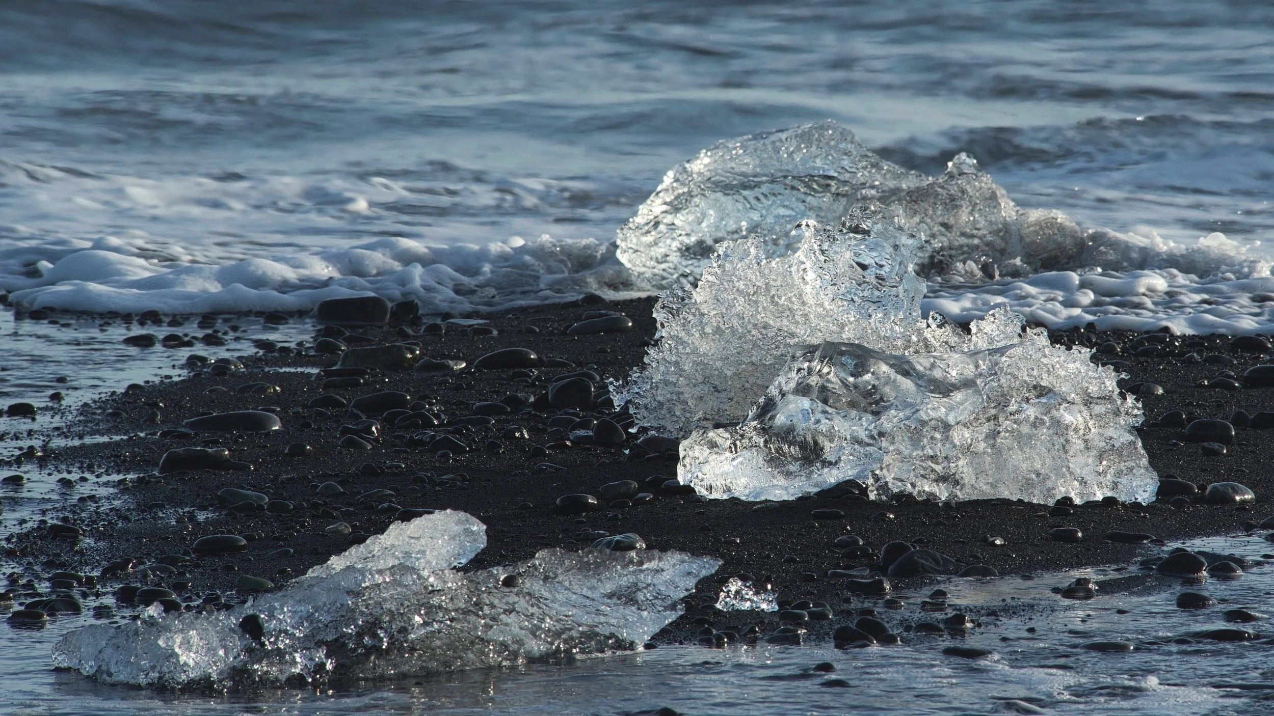 Plage de sable noir avec morceaux de glace et vagues de l'océan