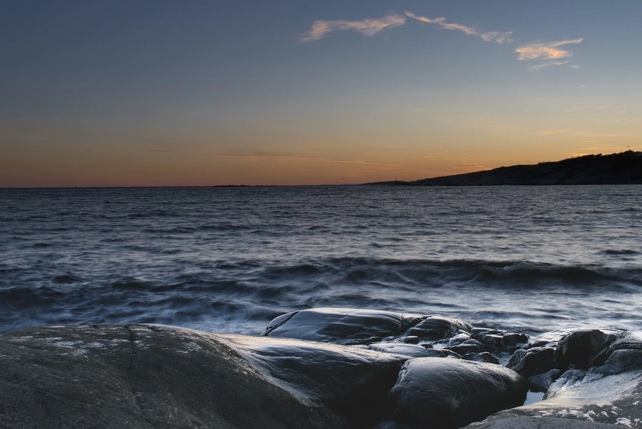 Coucher de soleil sur l'océan avec des rochers au premier plan.