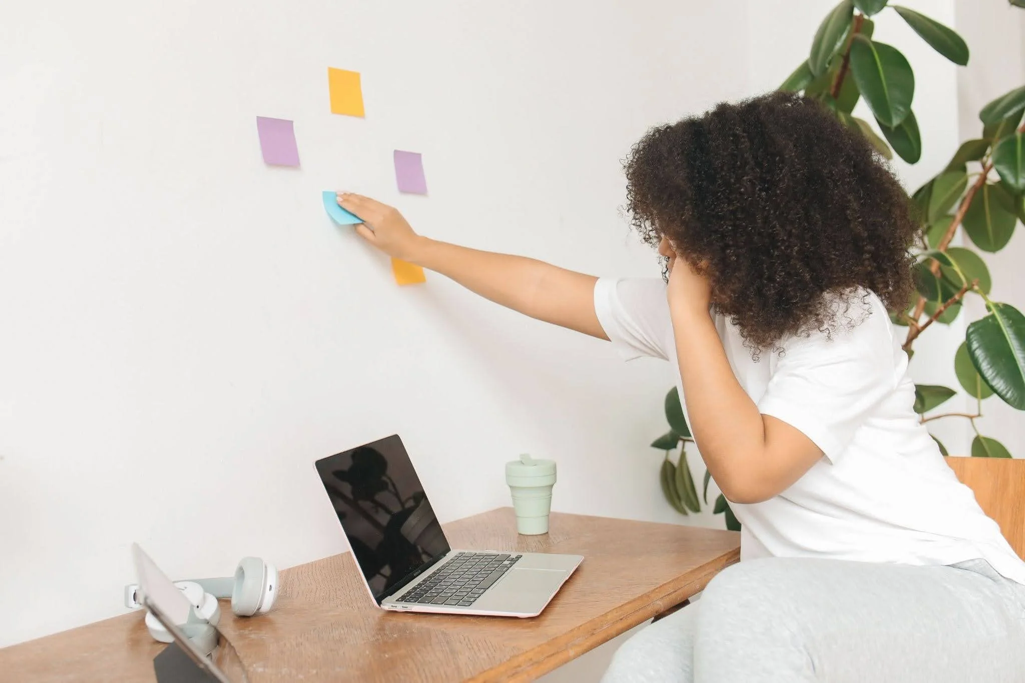 Young woman using sticky notes to organize tasks beside a laptop, illustrating ADHD and AuDHD planning challenges.
