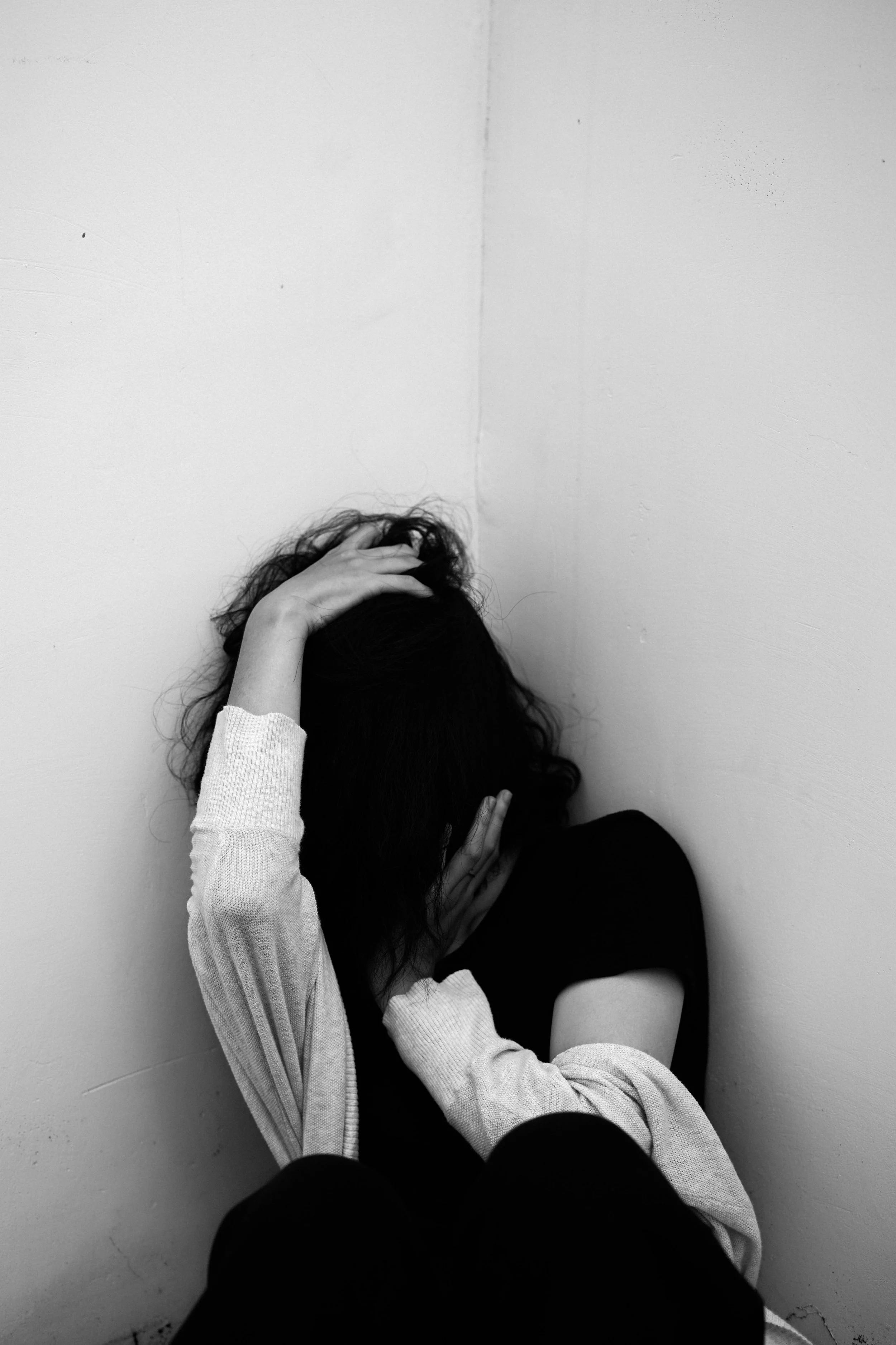 Person sitting against a plain wall, holding their head with one hand, in a black and white photo.