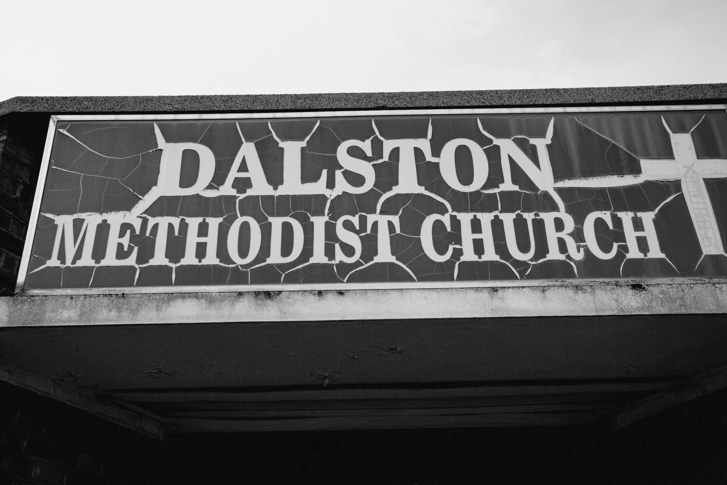 Sign for Dalston Methodist Church with cracked paint and dust on the edges.