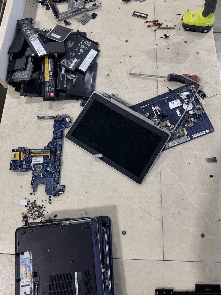 Disassembled laptop on a table with battery packs, tools, and internal components scattered around.