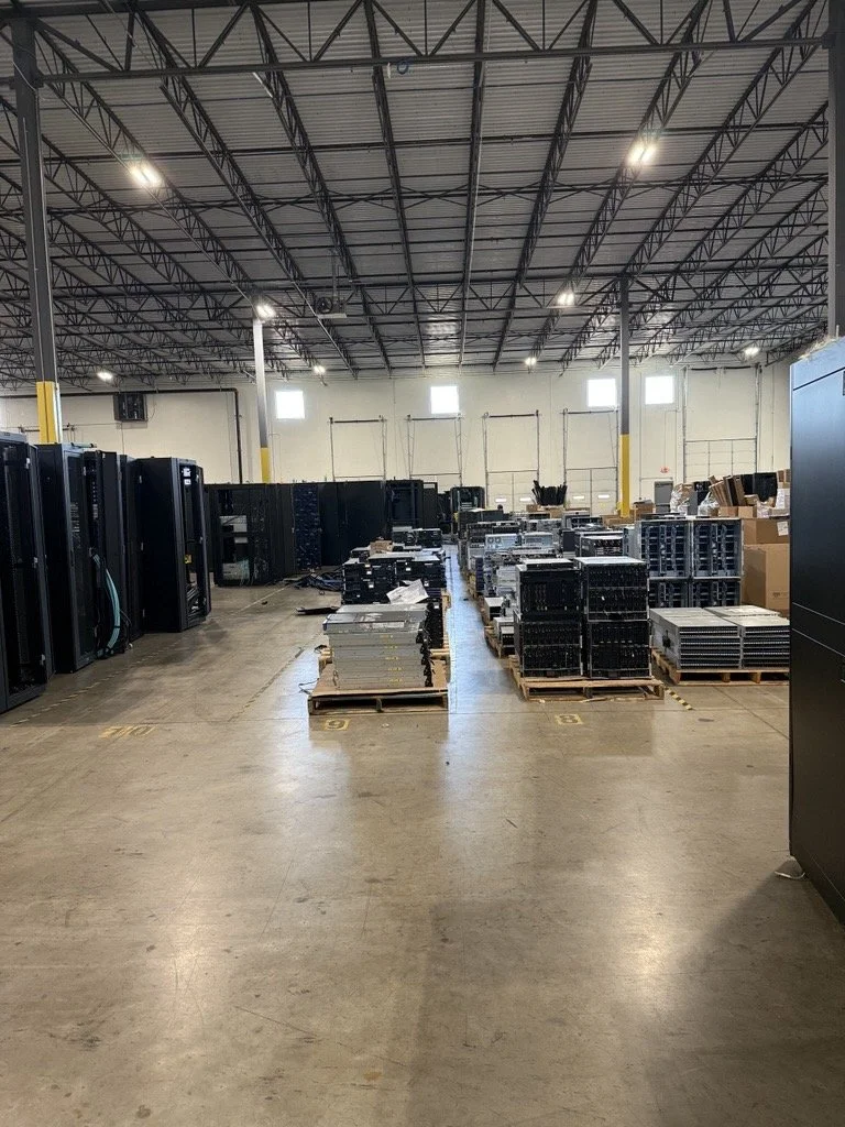 Warehouse with server racks and hardware equipment organized on pallets and shelves.