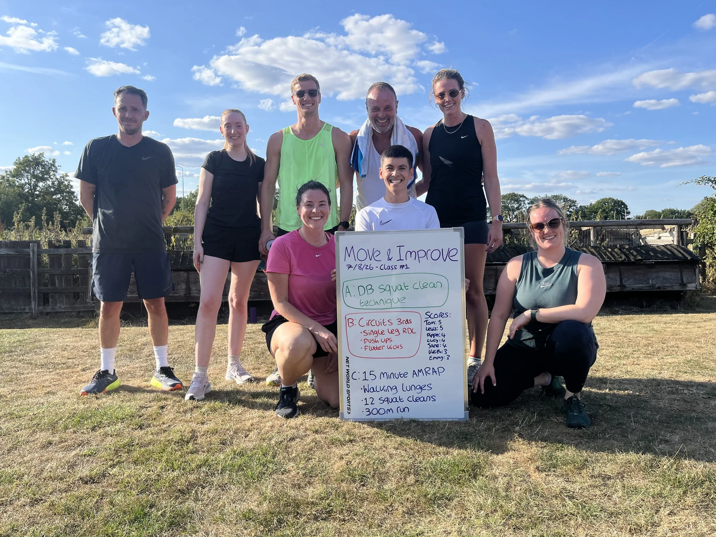 Group of eight people posing outside Box Trees Farm after completing a Move & Improve class. The whiteboard indicates the warm up, strength technique movement, circuit training, 15 minute workout of the day and cool down stretches.
