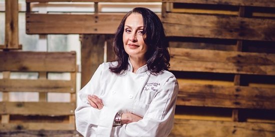 Professional chef posing with arms crossed in a kitchen setting, wearing a chef's coat.