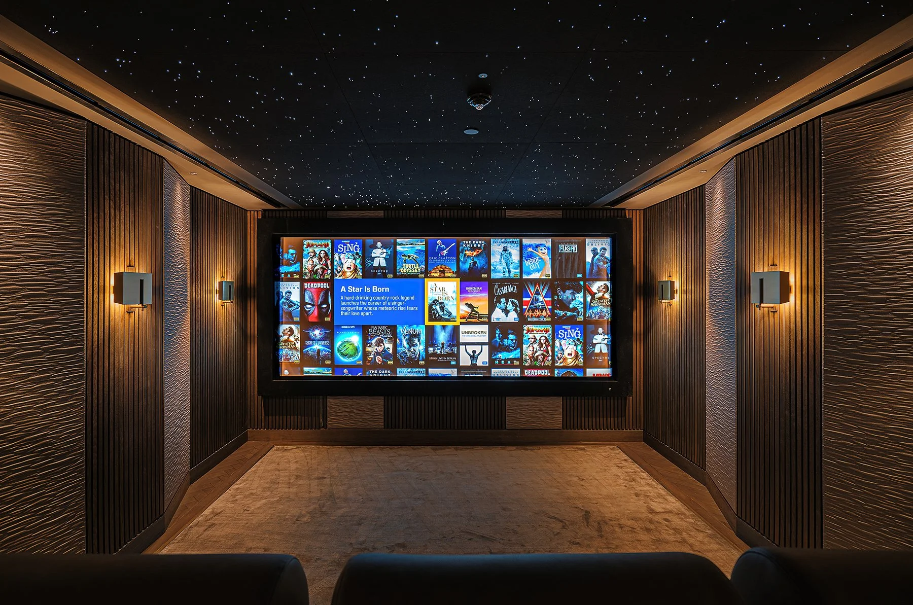 Modern home theater with large screen and movie selection, dim lighting, starry ceiling, and cozy seating area.