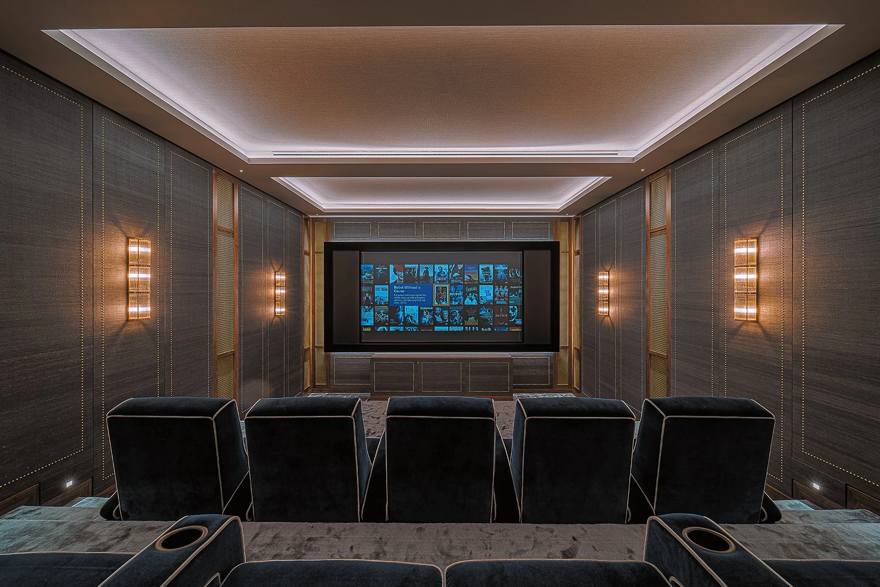 Luxury home theater with cushioned seating, a large screen displaying movie thumbnails, and modern wall sconces providing ambient lighting.