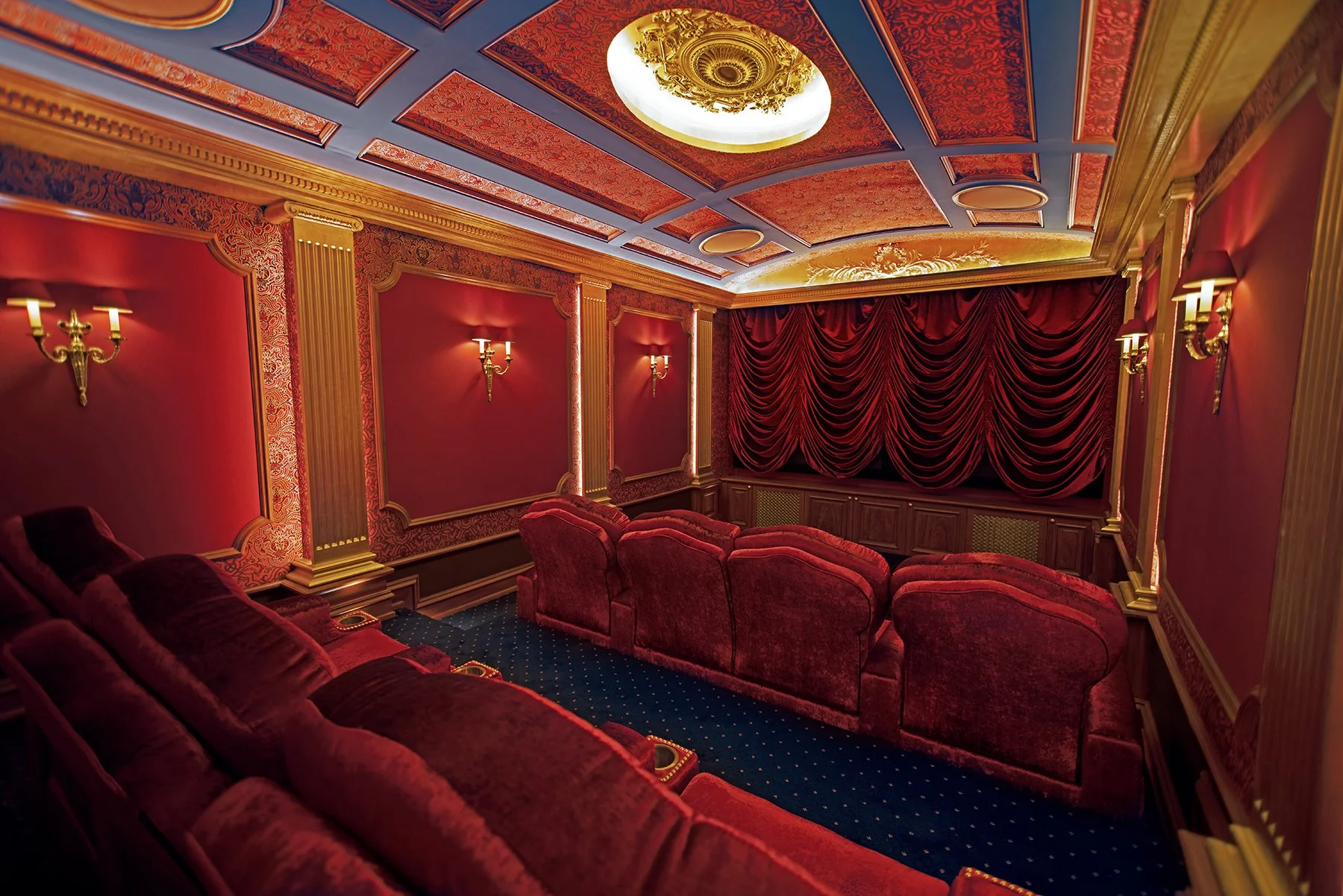Luxury home theater with red velvet seating, ornate gold-rimmed walls, and ceiling lights.