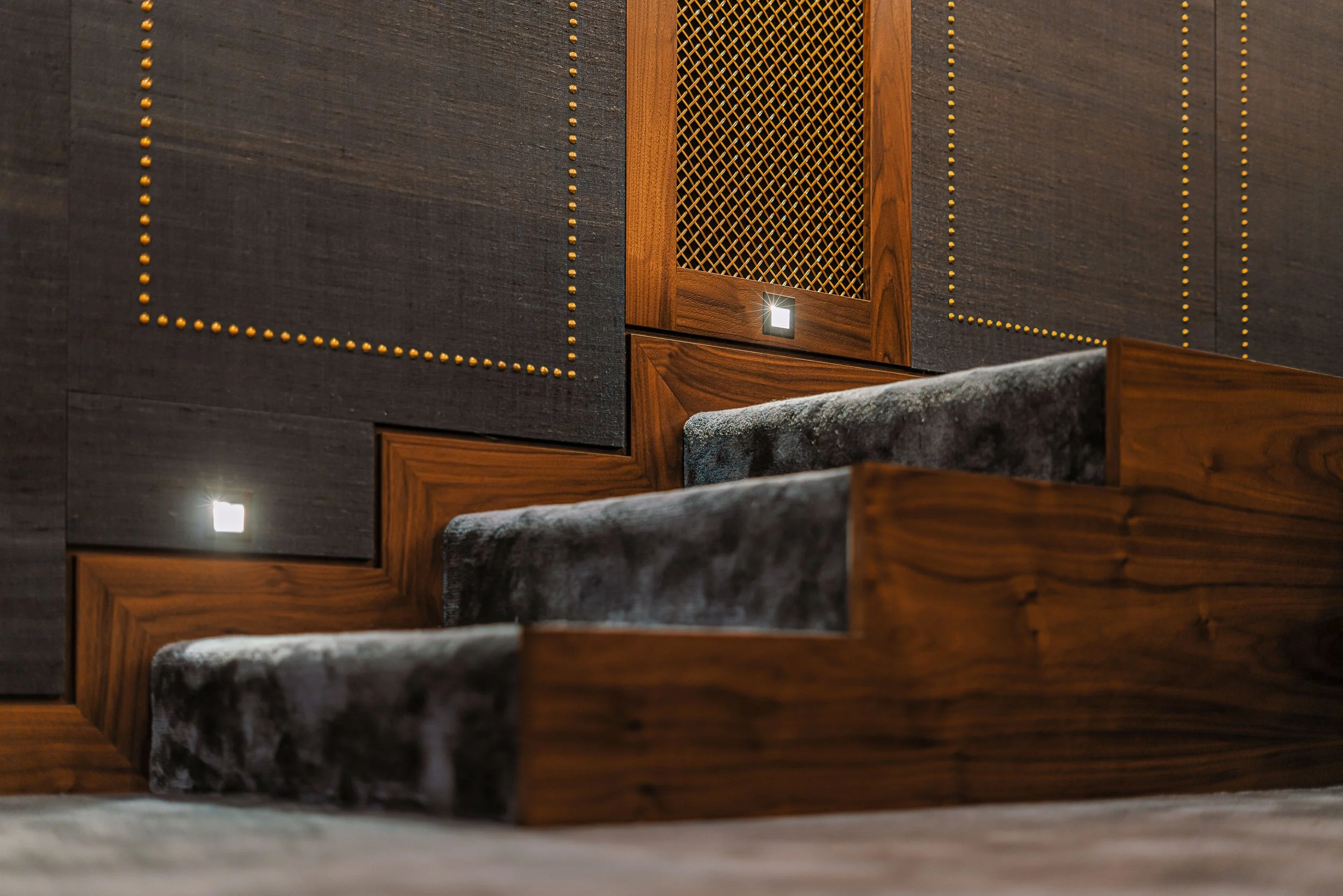 Close-up of a modern staircase with wooden panels and soft carpeted steps, featuring small recessed LED lights and decorative wall detailing.