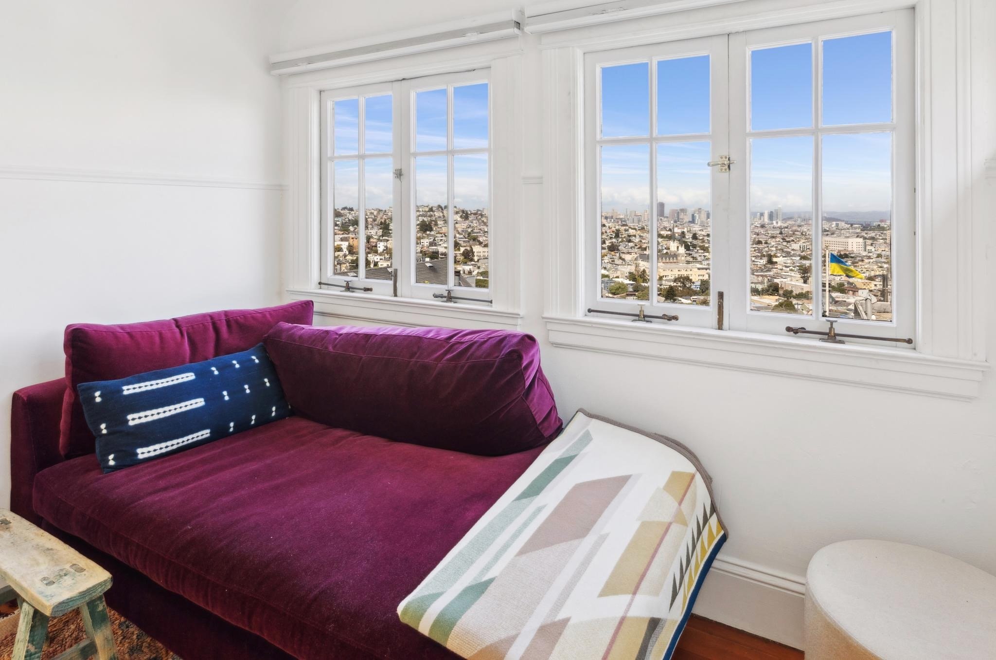 Cozy corner with a purple sofa and blue decorative pillow by a window with cityscape view