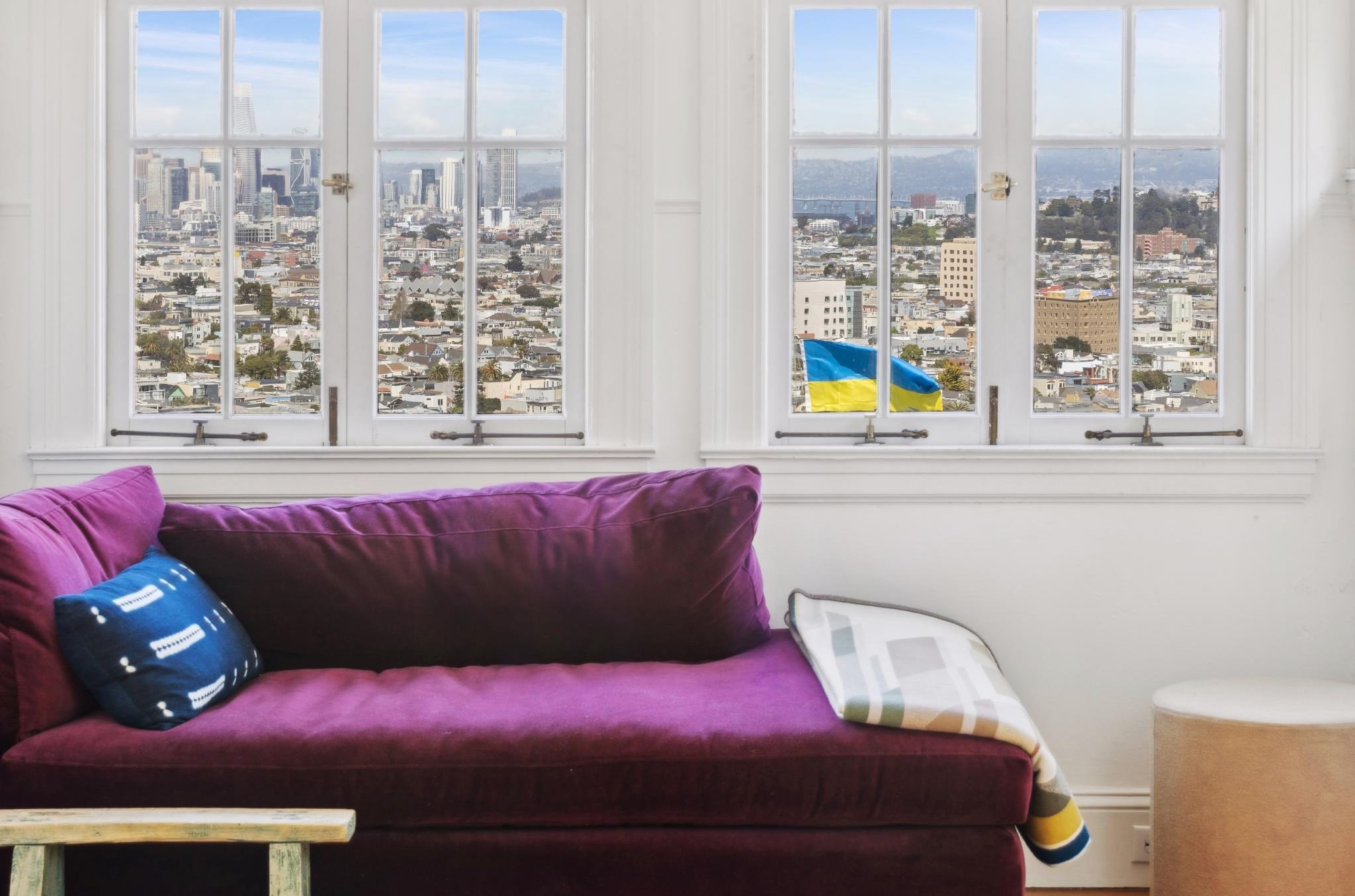 Room with a purple sofa and a large window showing a cityscape