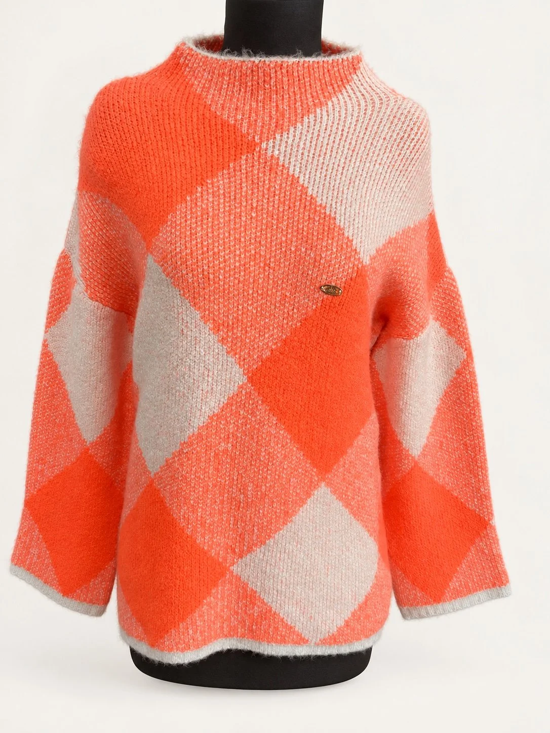 Coral and ivory argyle-knit sweater with long sleeves, displayed on a dress form.