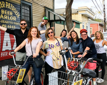 Group of seven people posing with shopping carts outside a store, smiling and making playful gestures, with a yellow building and signage in the background.