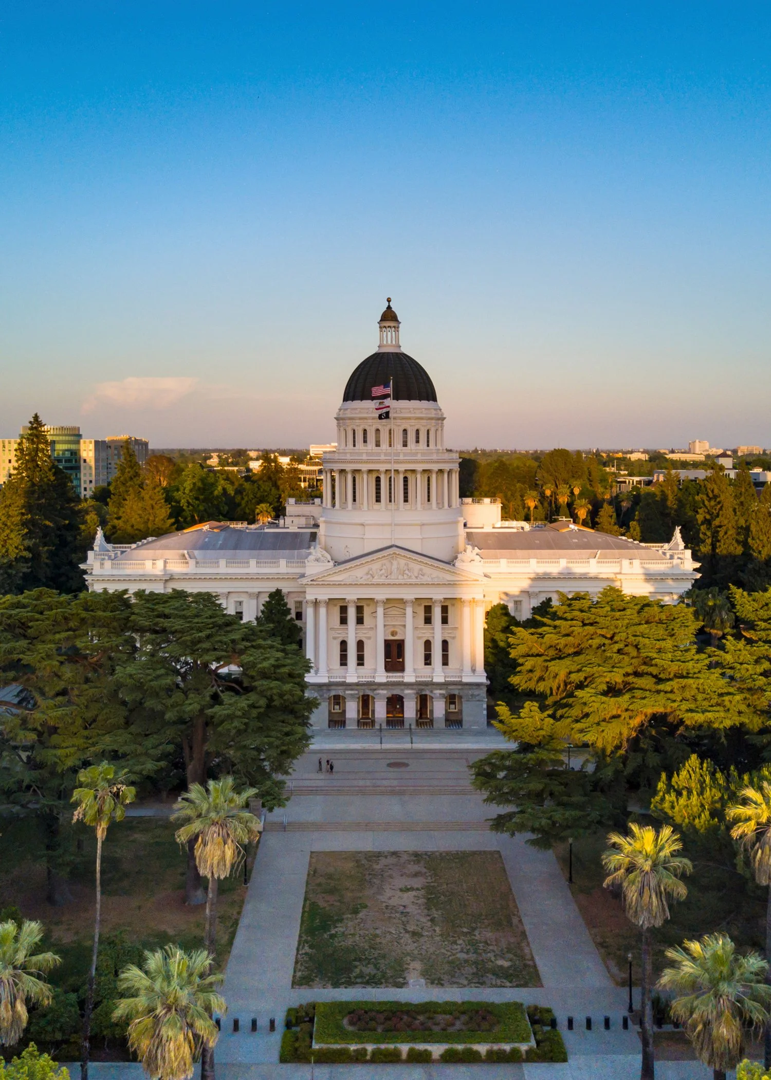 California State Capitol building with a dome, surrounded by trees and gardens at sunset.