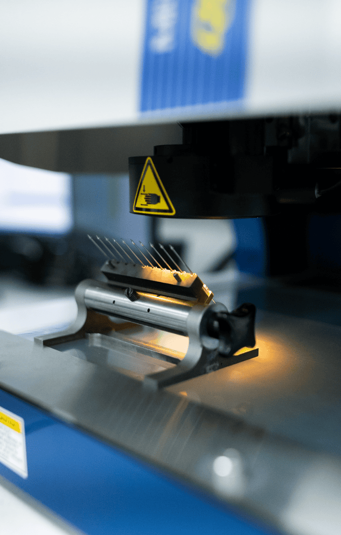 Close-up of a machine with pointed metal needles illuminated by a small light.