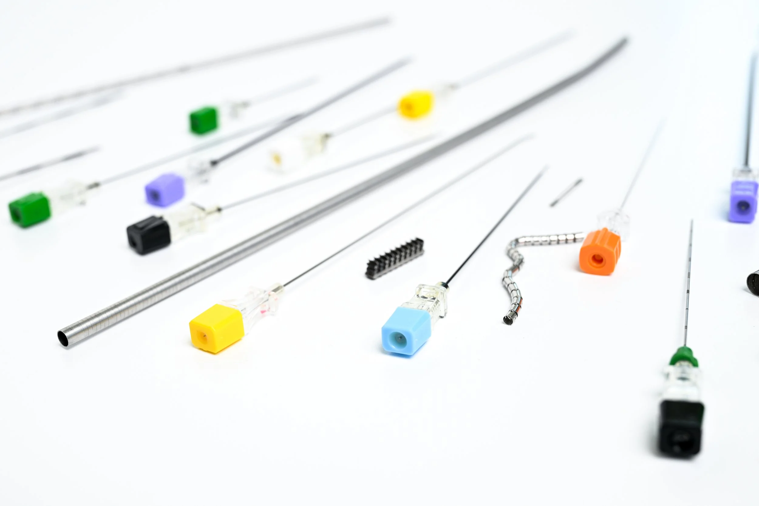 Assorted medical needles, metal tubing, and small components arranged on a white surface.