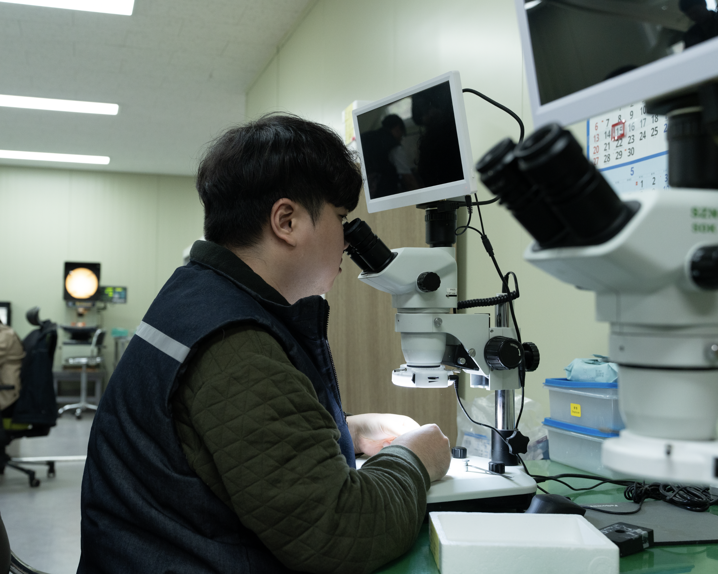 Technician inspecting a precision medical component under a microscope during medical device manufacturing.