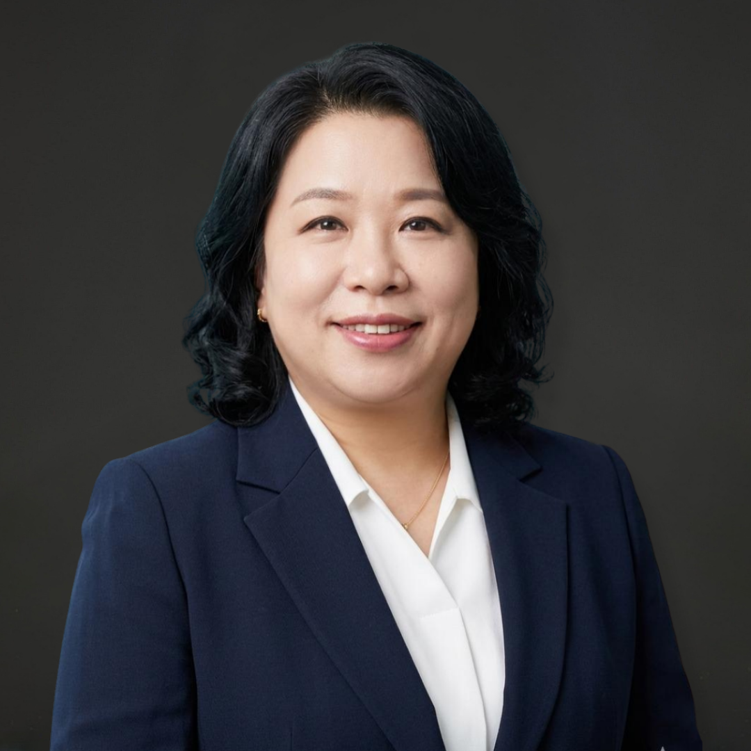 Professional woman with shoulder-length black hair, wearing a dark navy blazer and white shirt, smiling against a dark gray background.