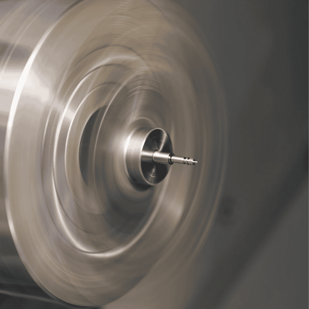 A metal lathe spinning and shaping a small cylindrical workpiece in the center.