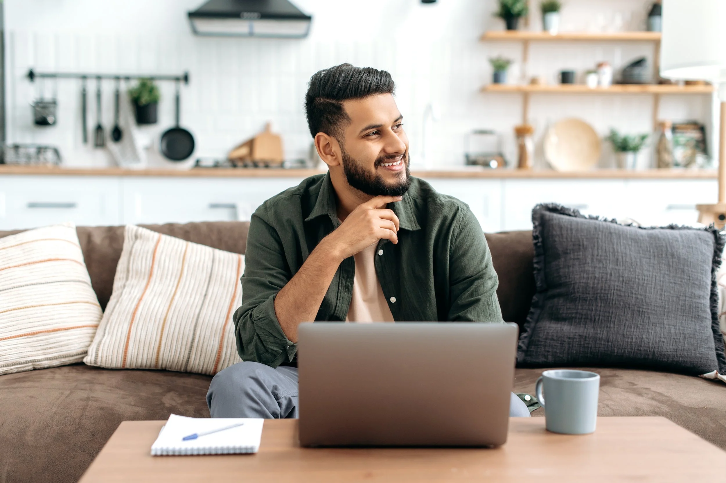 Image of a thoughtful young man using a laptop in his living room—representing the flexibility, comfort, and accessibility of online therapy for individuals seeking mental health support from home