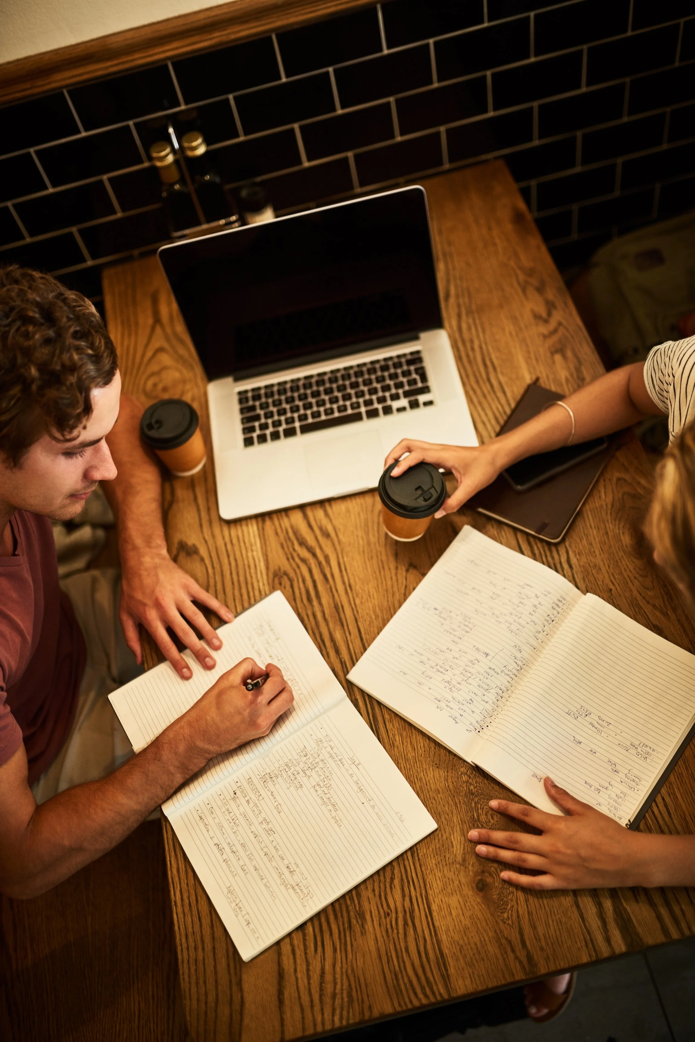 Two people studying together at a café table representing collaboration learning and the thoughtful research behind Guidance Teletherapy’s entertainment industry consultation services for accurate mental health representation