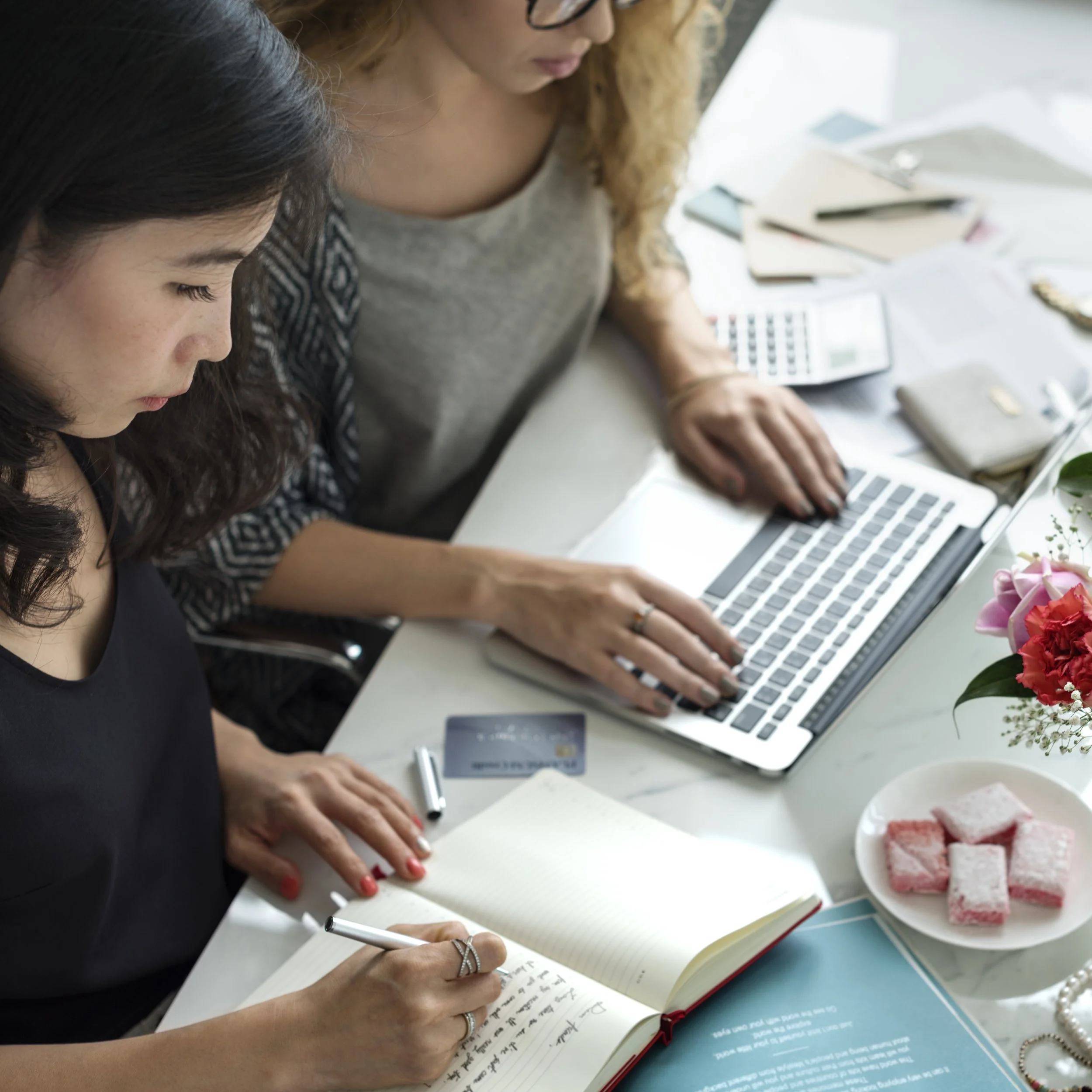 Image of two women collaborating on a laptop and taking notes, representing Guidance Teletherapy’s Entertainment Industry Consultation services
