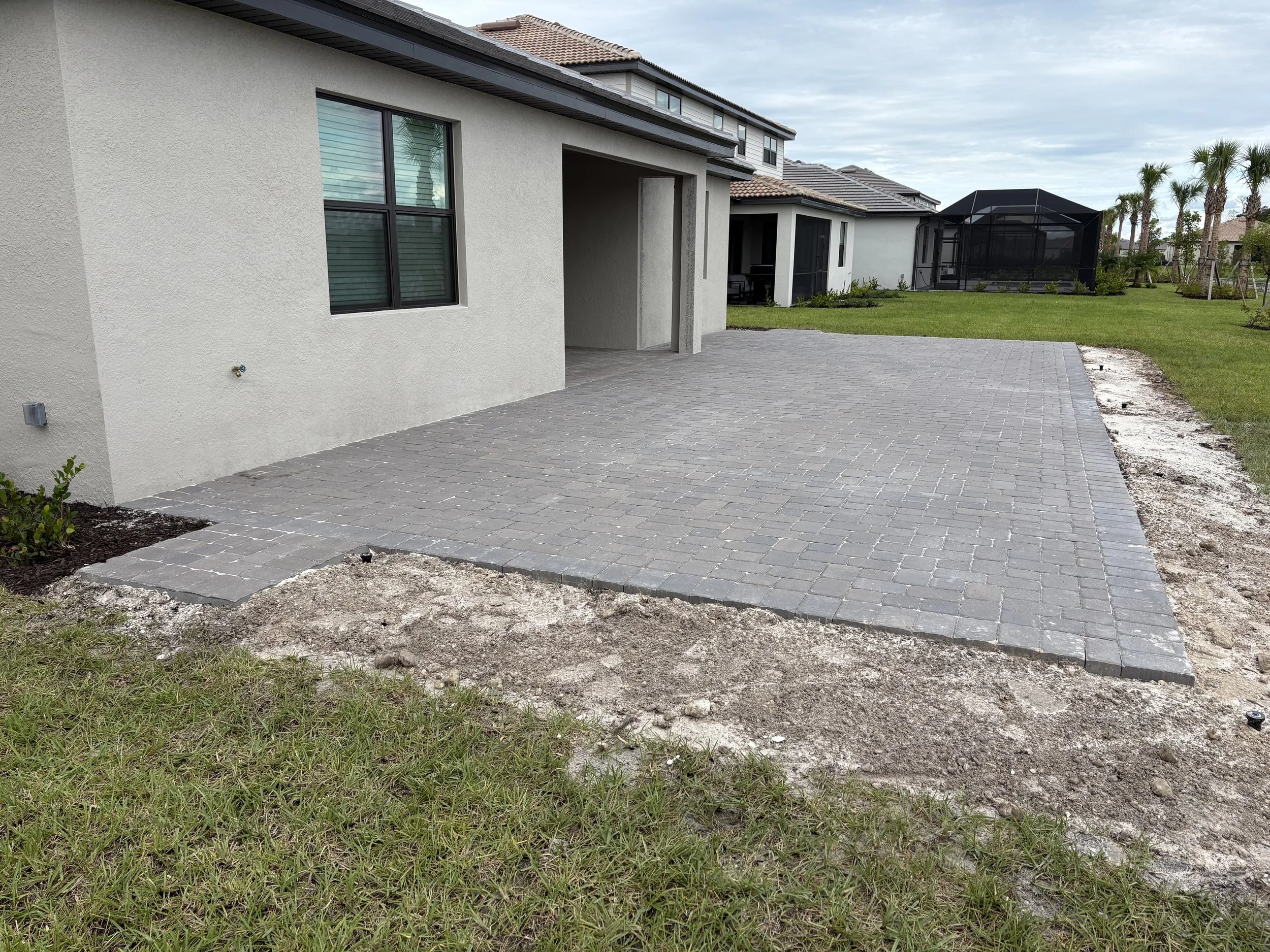 Newly paved stone patio area in backyard with grass and neighboring houses visible.