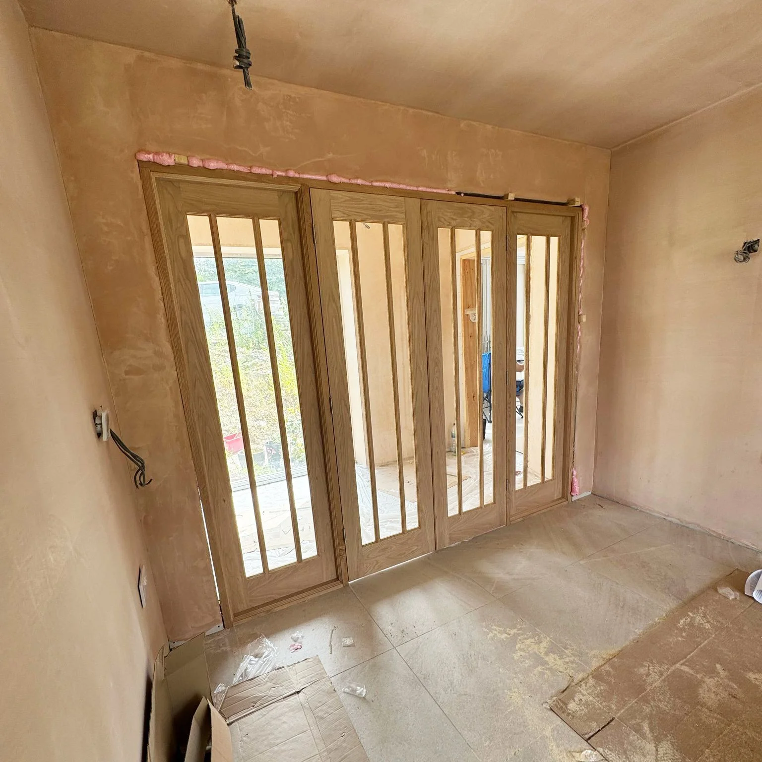 Construction site with wooden folding doors and unfinished plaster walls.