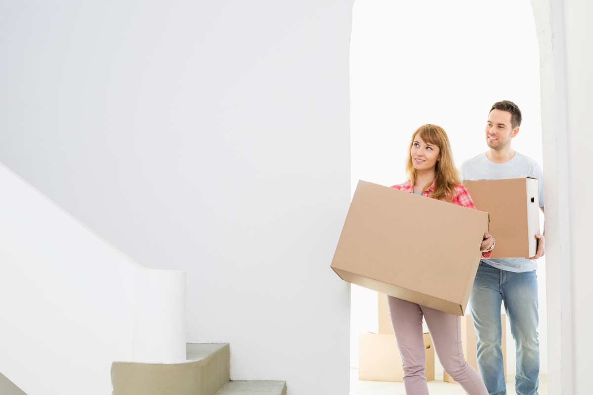 Smiling couple carrying moving boxes into a bright new home.