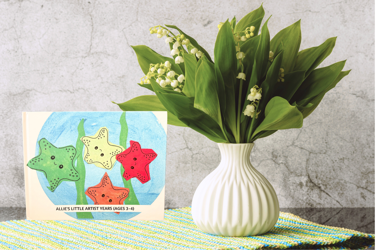 Children’s artwork turned into a custom Artkive book displayed beside a vase of fresh flowers in a calm, styled home setting
