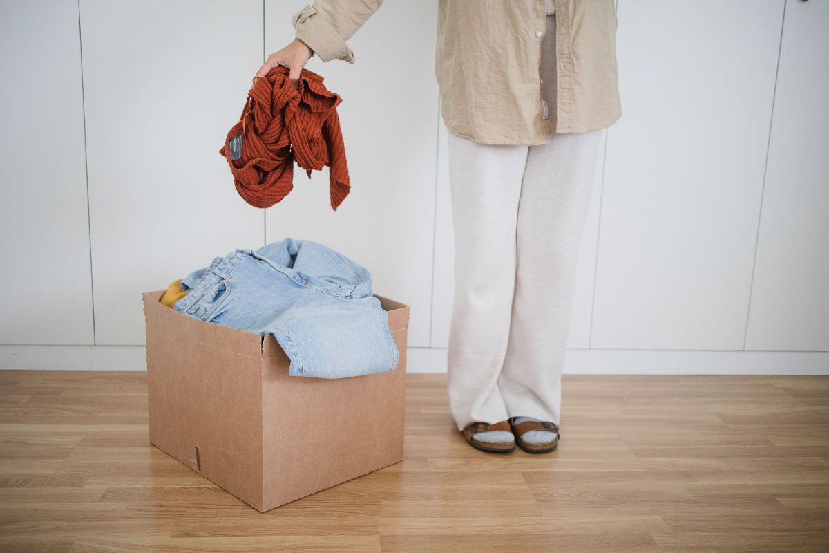 Person decluttering and placing clothes into a donation box at home.