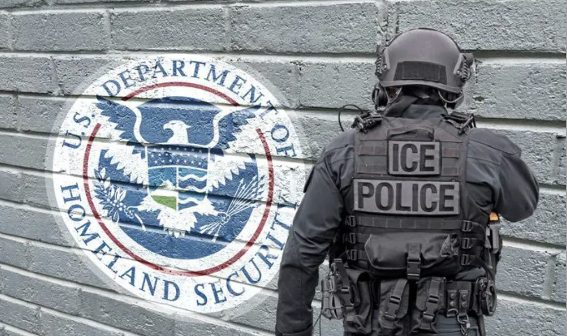 A federal officer standing next to a U.S. Department of Homeland Security emblem on a brick wall, with the officer wearing tactical gear labeled ICE Police and a helmet, Staunton Security, Stauntonsecurity.com