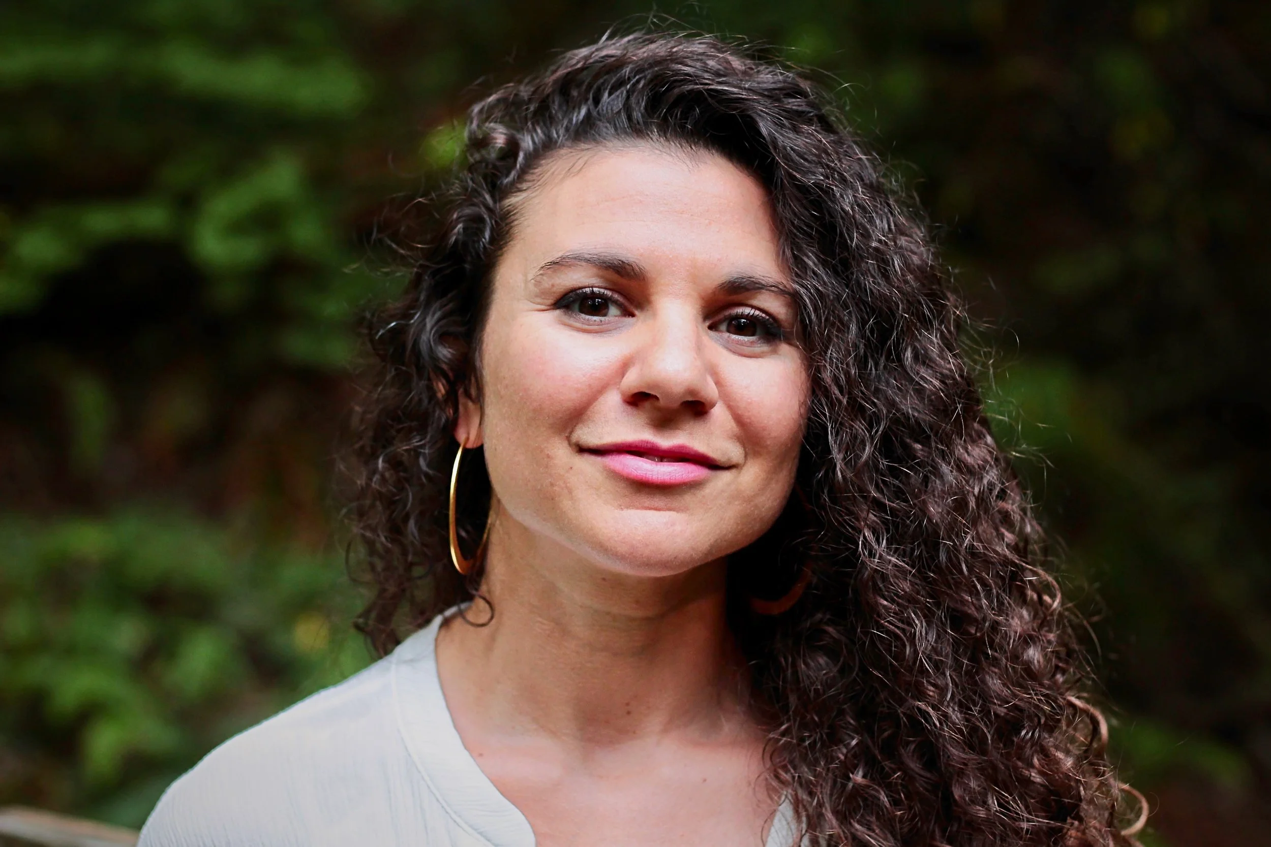 Woman with curly hair and hoop earrings smiling outdoors.
