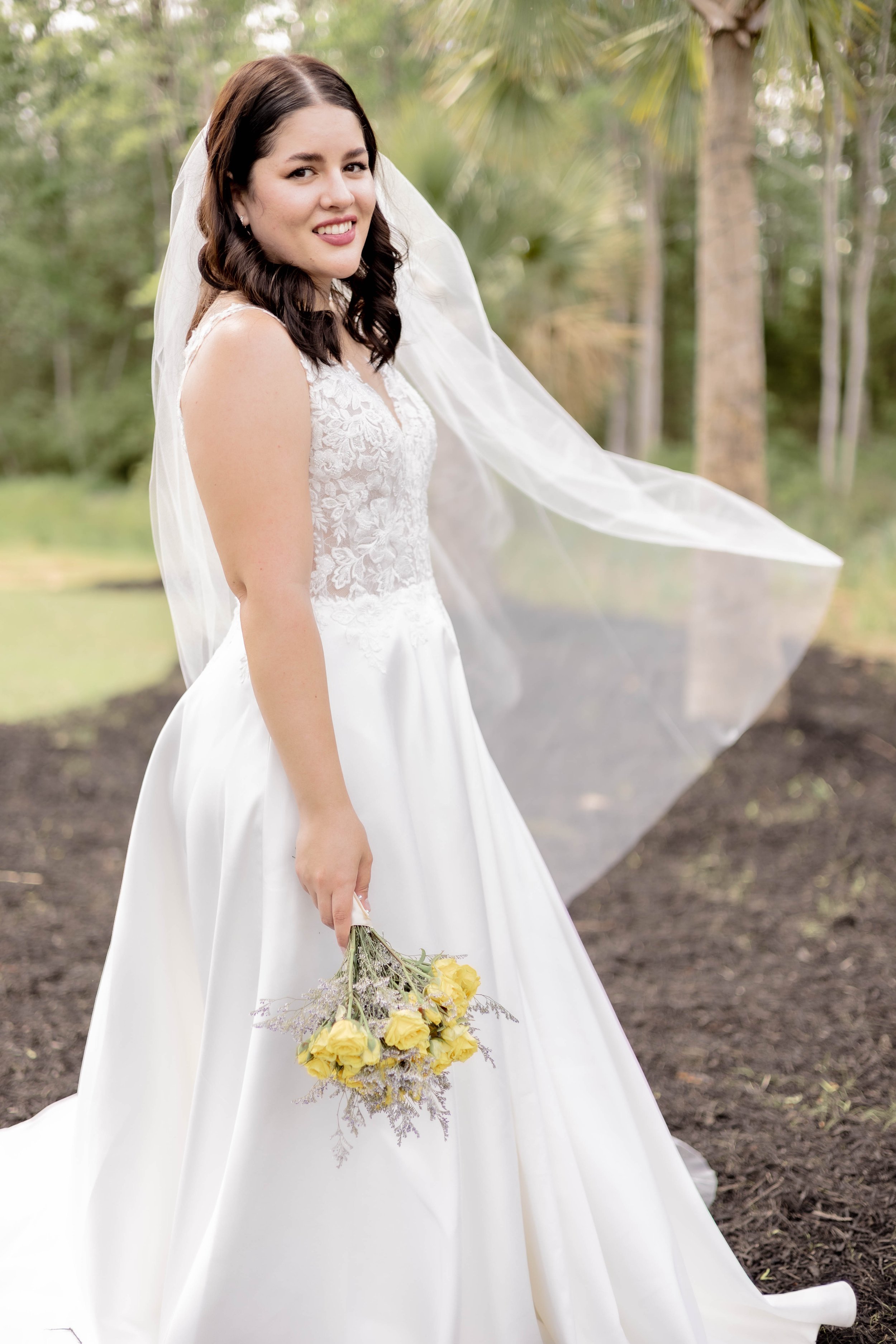 Bride in white gown holding yellow flowers outdoors