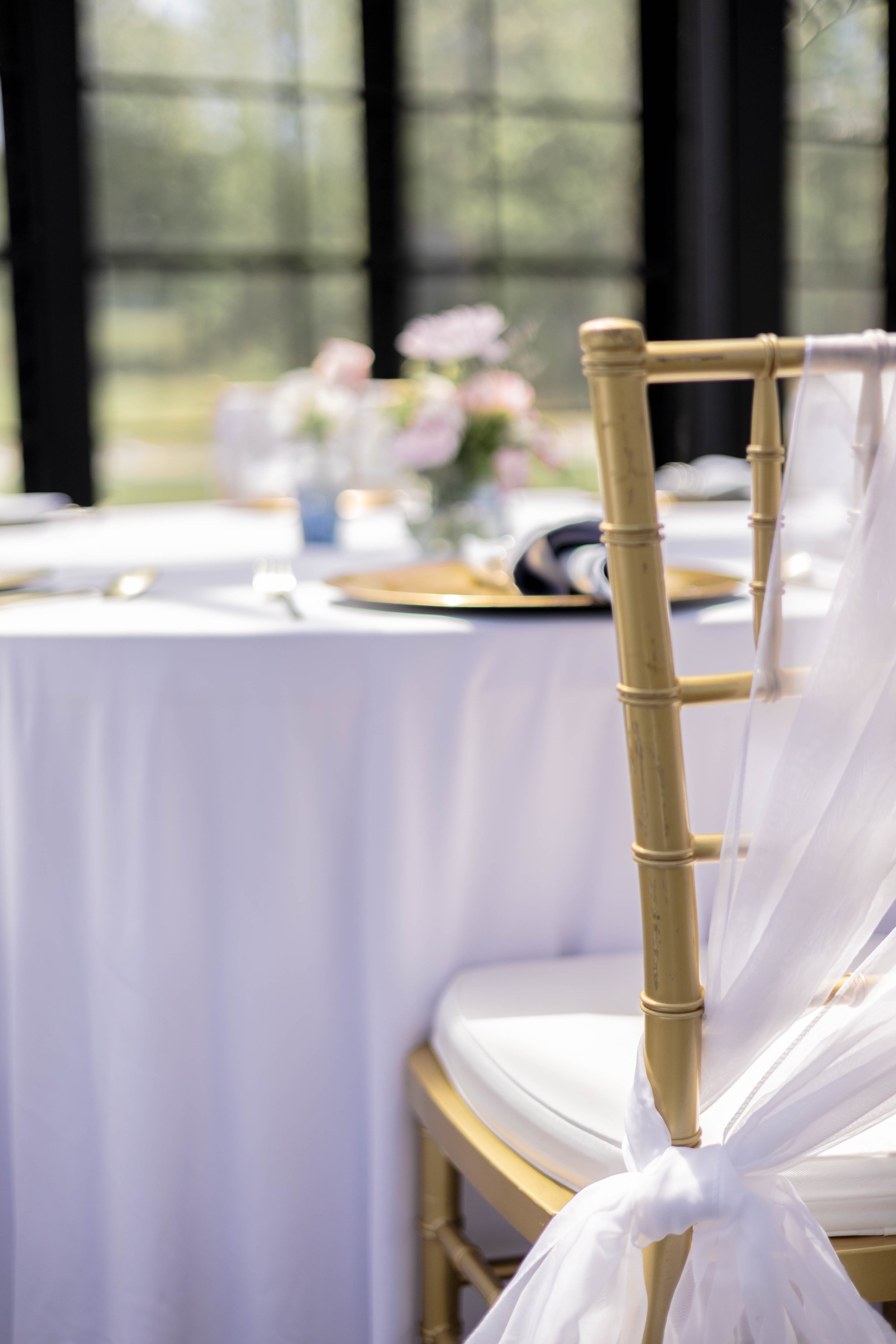Elegant table setting with gold chair and white tablecloth, decorated with floral centerpieces.
