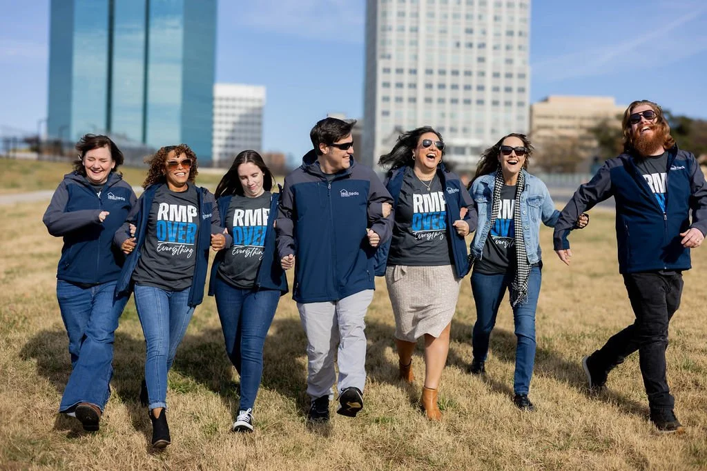 Group of seven diverse people walking together outdoors in Winston-Salem, NC, all smiling and wearing matching navy jackets and black T-shirts with blue and white text.