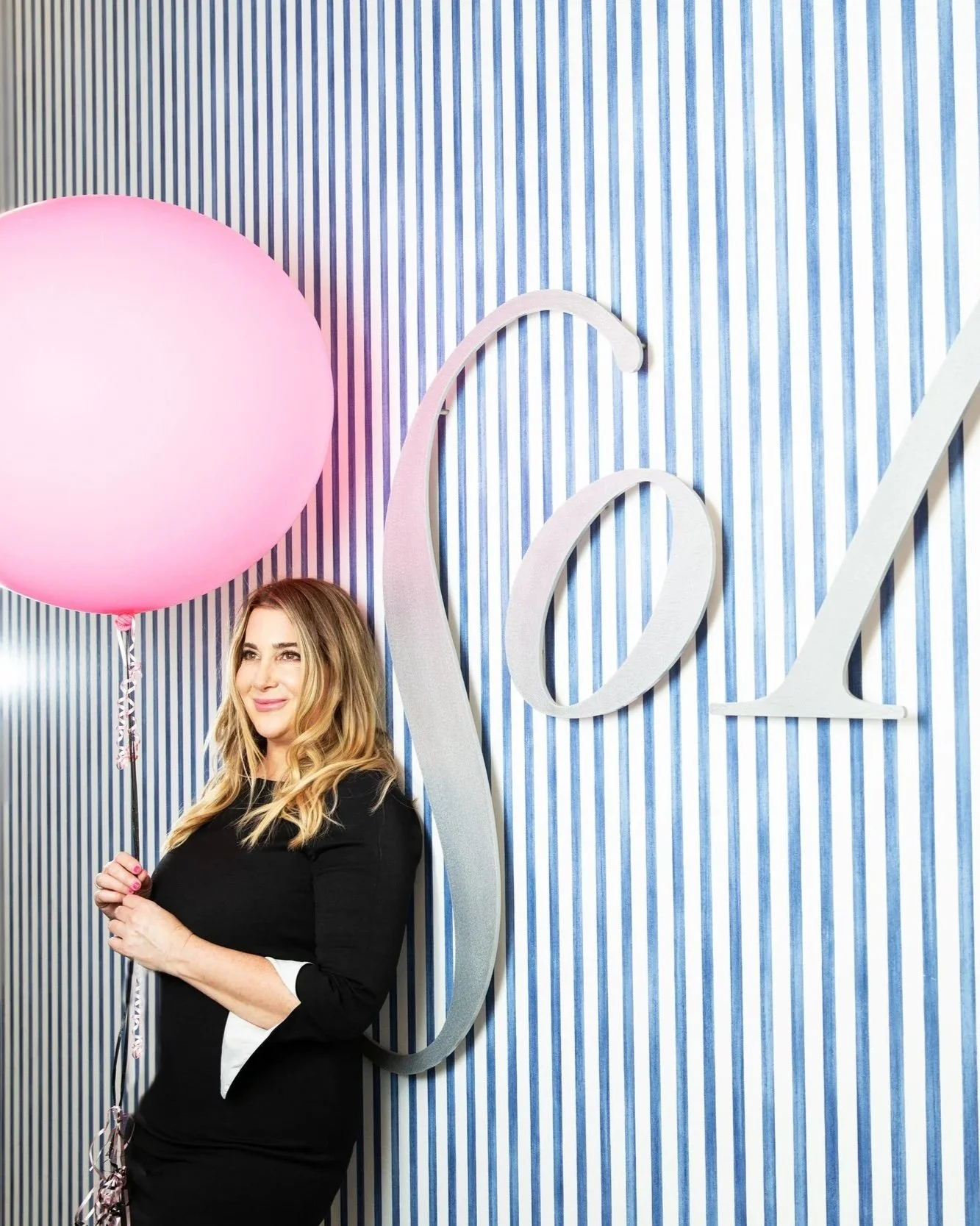 Libbey standing at the entrance of the Sola Salon with a pink balloon for her first anniversary in 2019.
