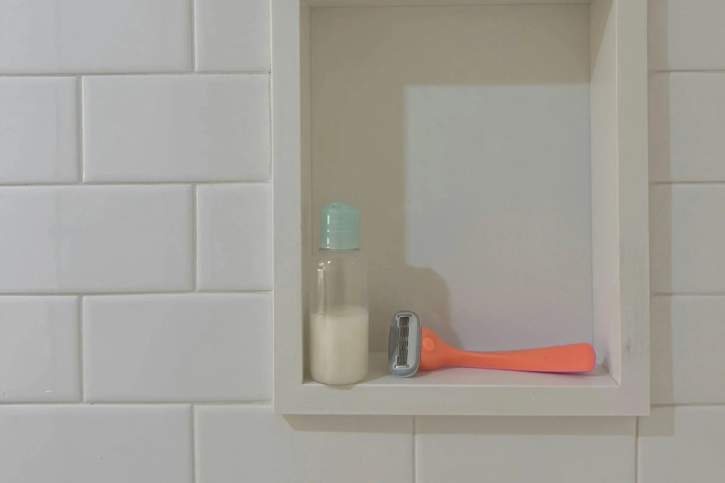 Organge razor and a travel bottle of shampoo in a shower wall