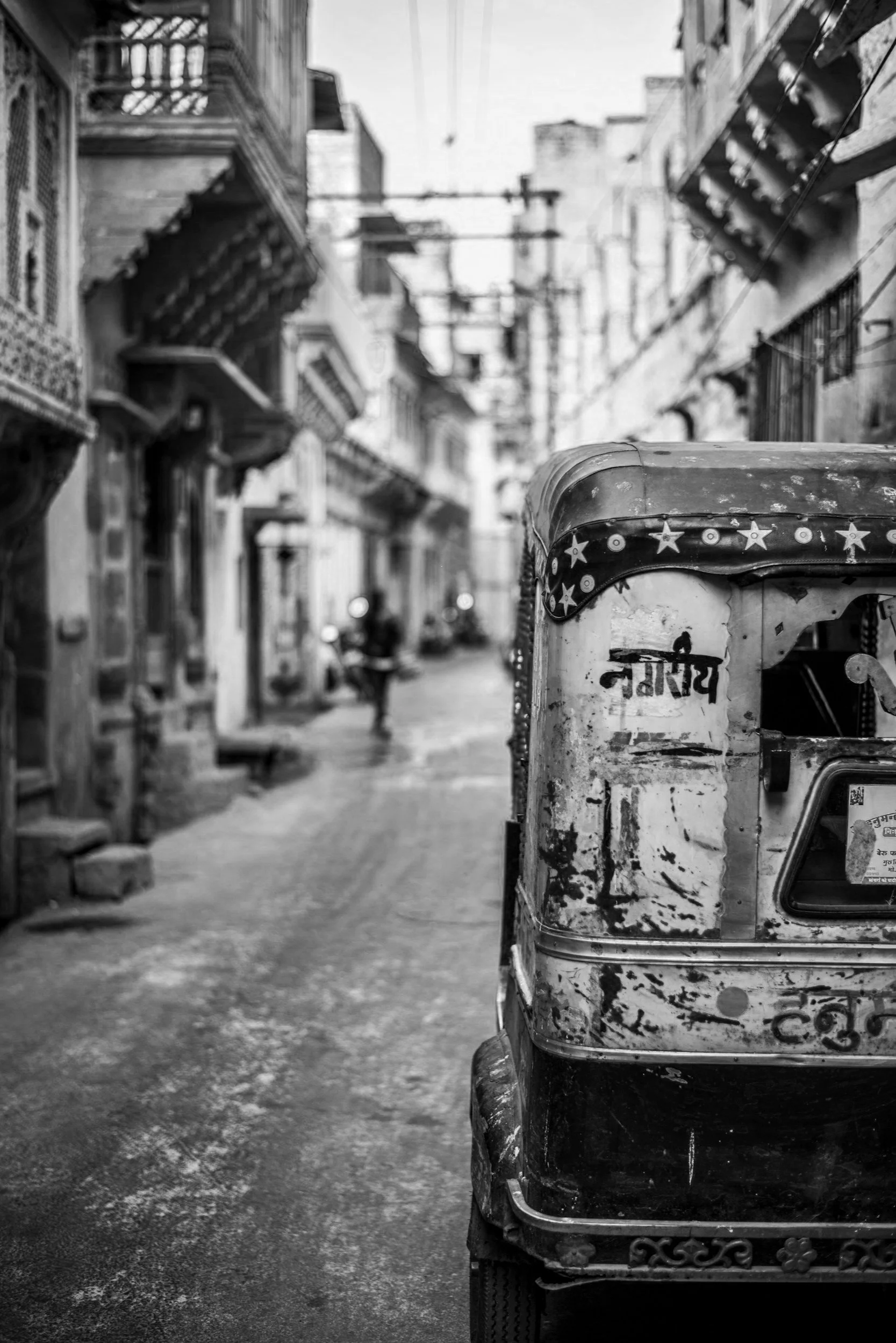 Black and white image of an auto rickshaw parked in a narrow, old city street with traditional architecture.