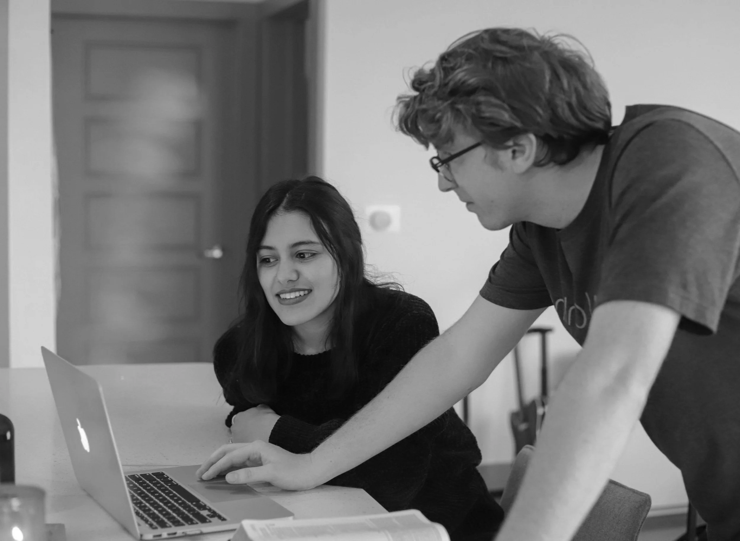 Two people looking at a laptop screen, one seated and the other standing, discussing or collaborating.