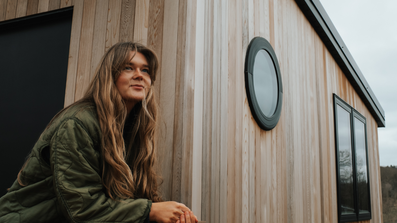 A mobile sauna is in the background with a woman smiling softly in the forefront.