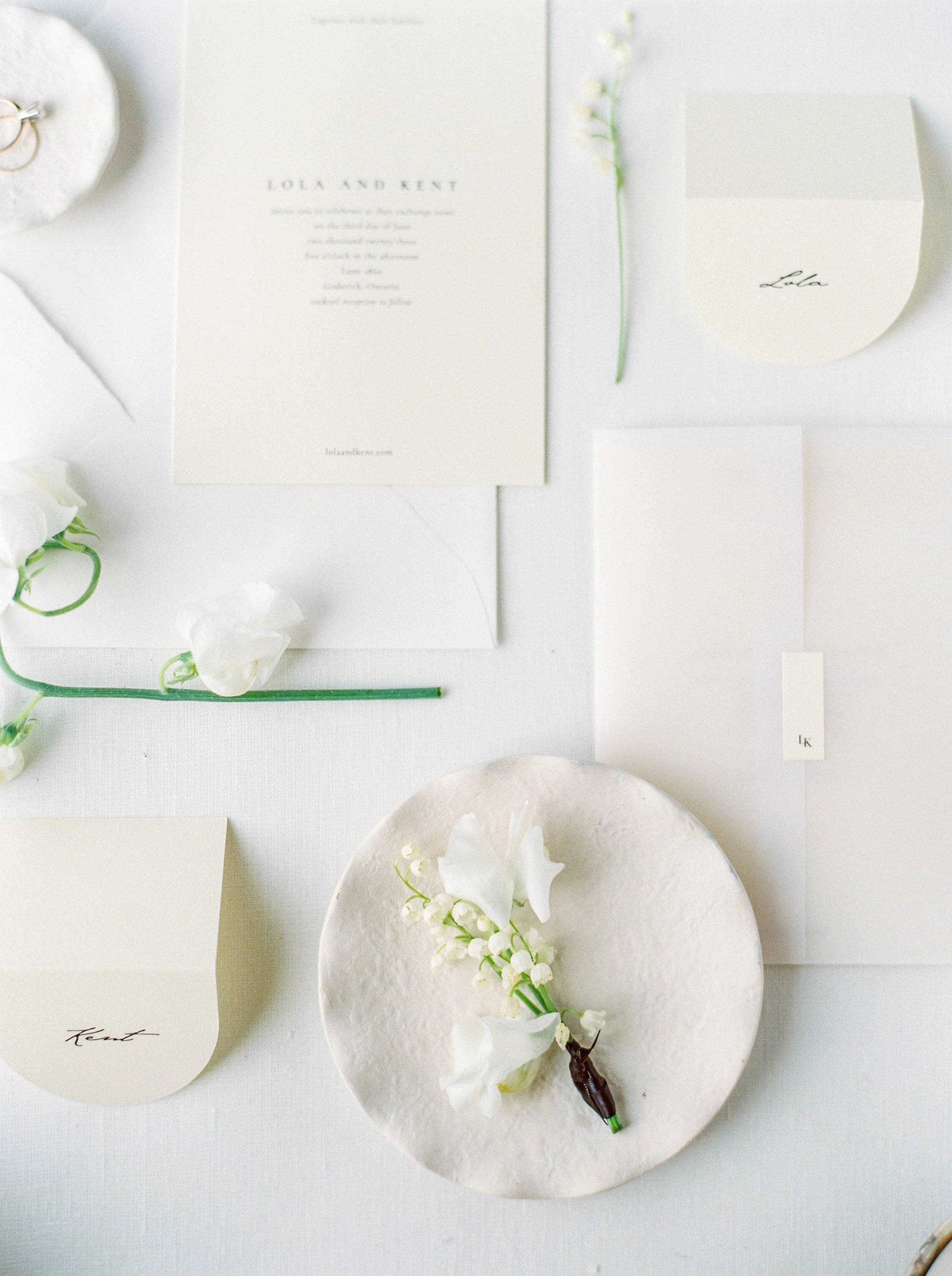 Flat lay of wedding stationery and floral decor on a white surface, including invitation cards, envelopes, and white flowers.